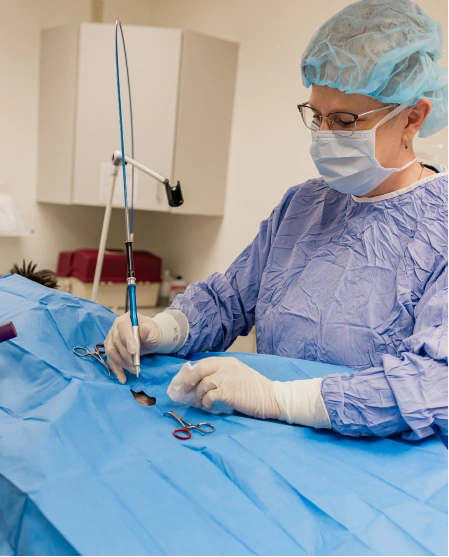 A surgeon in blue scrubs, mask, and cap performing surgery on a draped patient with surgical instruments.