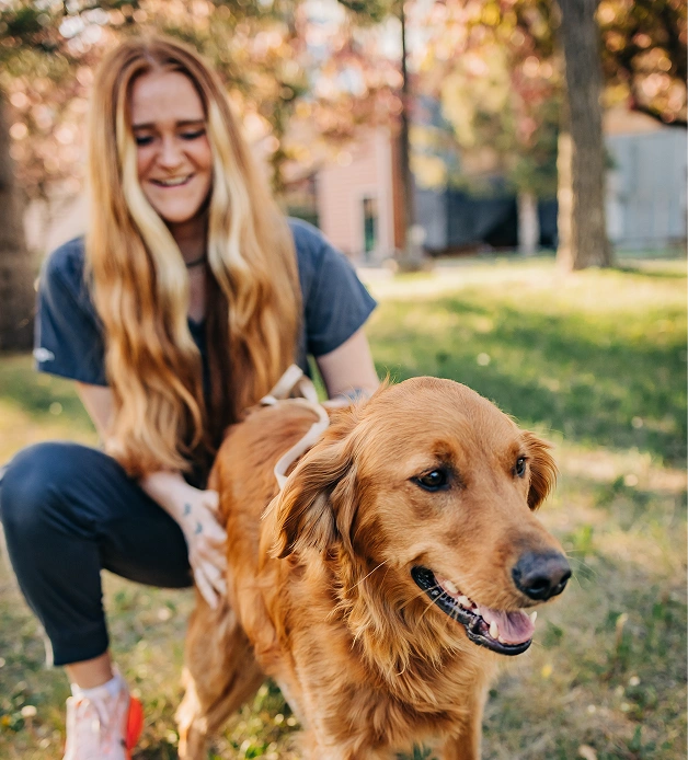 A staff member kneeling and smiling while petting a golden retriever outdoors.